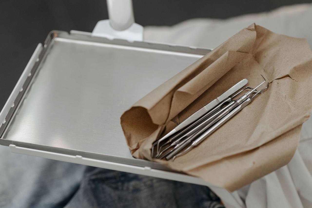 Bộ dụng cụ nha khoa nằm trong gói giấy nâu vừa mở, đặt trên khay inox cạnh ghế điều trị