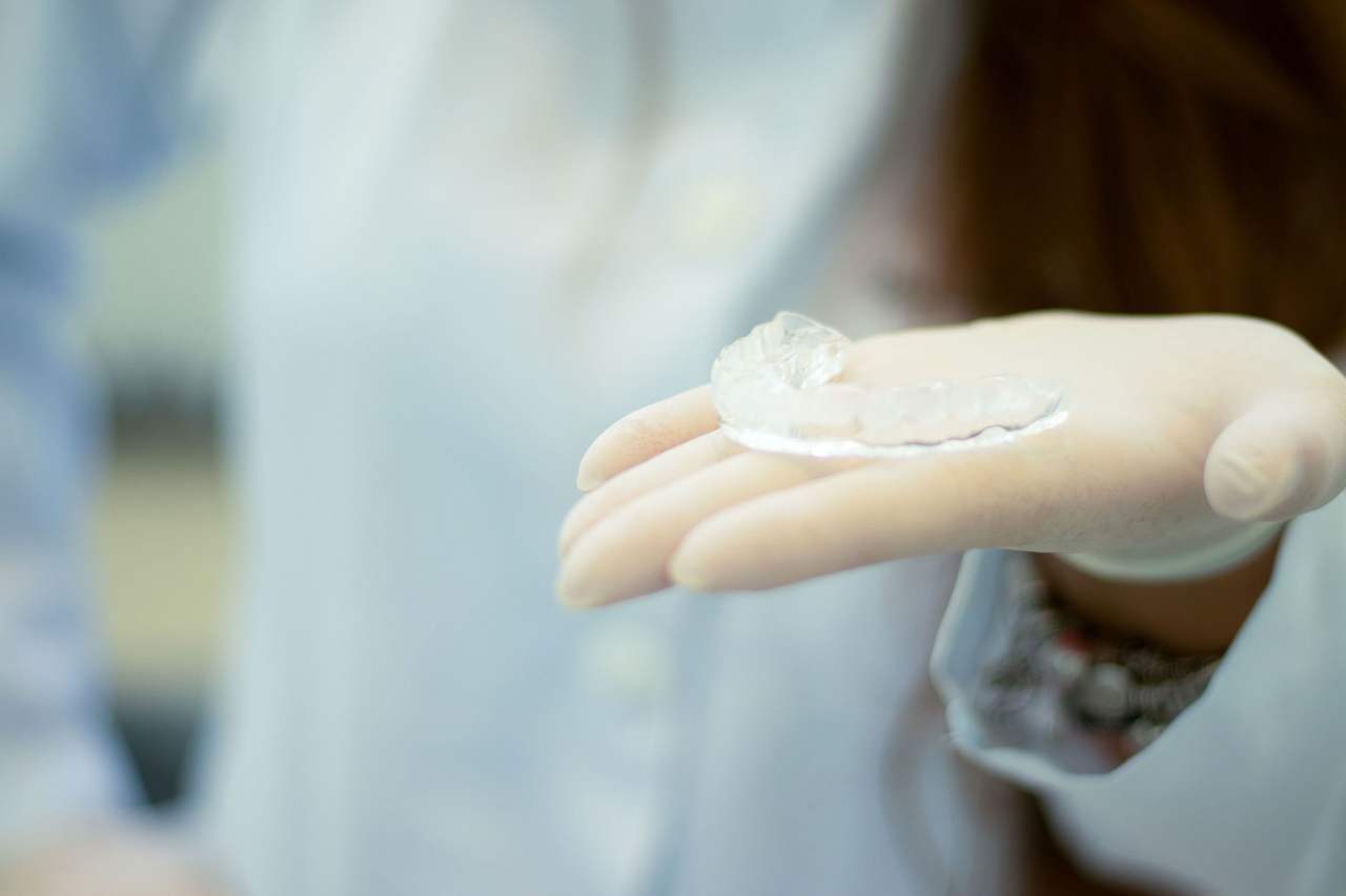 Một bàn tay đeo găng đặt khay nhựa trong suốt trên lòng bàn tay, hậu cảnh áo blouse trắng mờ